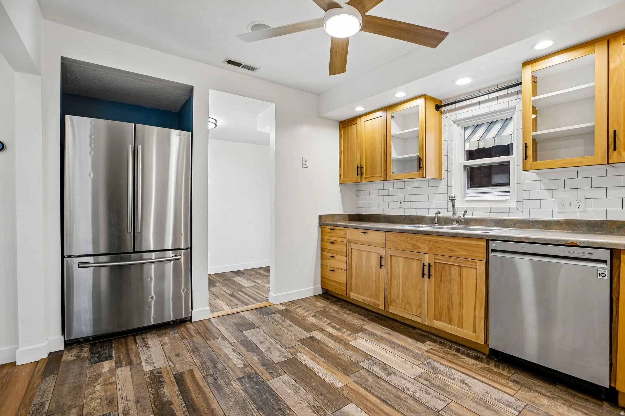Kitchen featuring wood-finish flooring, natural wood cabinetry, subway tile backsplash, and stainless steel appliances