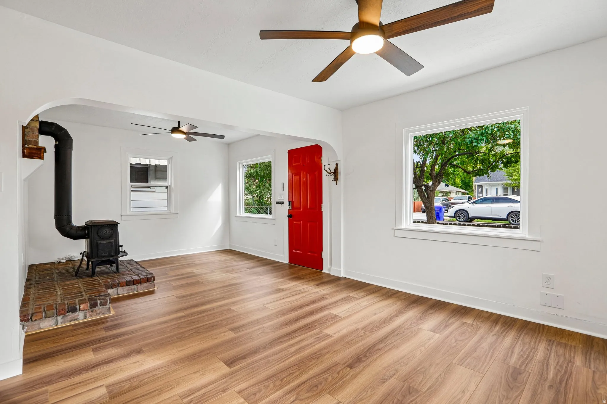 Wood-finish flooring, ceiling fans, red paneled door, and a brick hearth with a cast iron stove