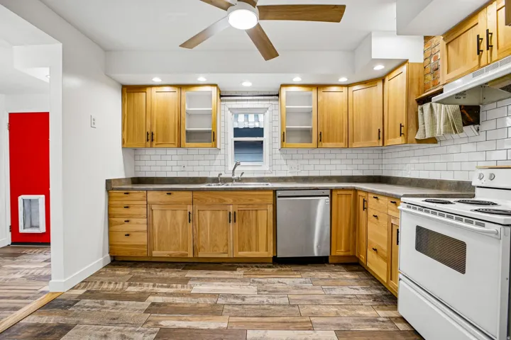 Kitchen featuring wood-finish flooring, wood cabinetry, subway tile backsplash, and a stainless steel dishwasher