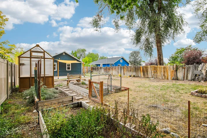 Expansive backyard featuring a greenhouse structure, raised garden beds, and a combination of wood and chain-link fencing