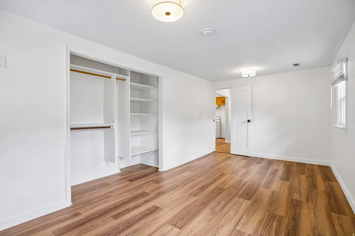 Wood-finish flooring, built-in closet organization, contemporary ceiling light fixture, white walls, and a window with blinds