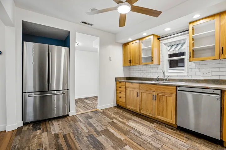 Kitchen featuring wood-finish flooring, natural wood cabinetry, subway tile backsplash, and stainless steel appliances