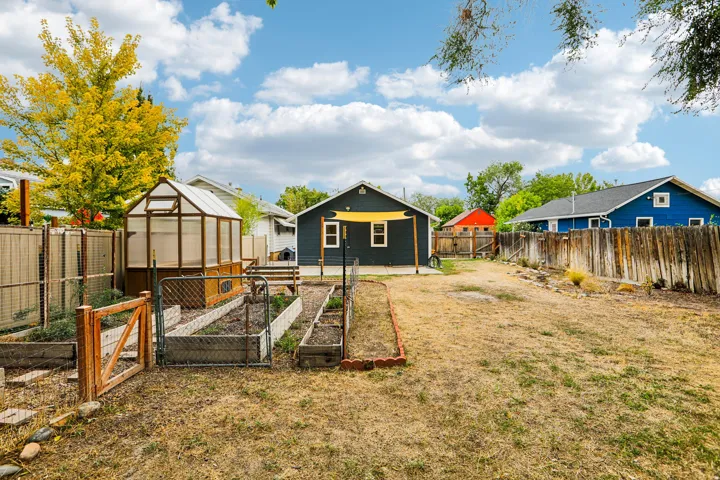 Spacious fenced yard featuring a greenhouse structure, multiple raised garden beds, and a back patio area with a sunshade