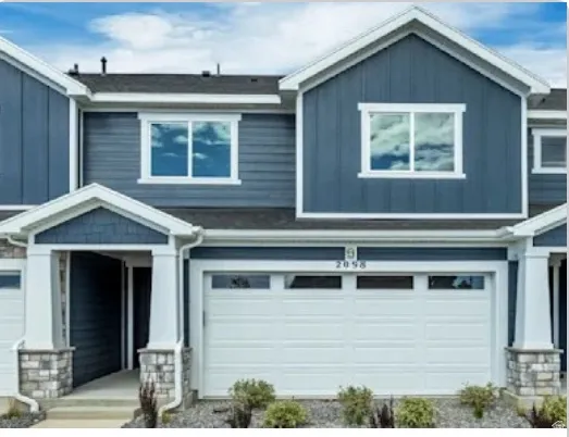 Contemporary exterior with blue siding, white trim, stone-accented columns, a recessed entry, and a paneled garage door with transom windows. This home is under construction. Pictures are of a similar home.