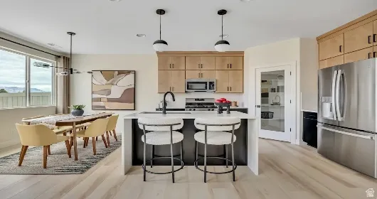 Open-concept kitchen and dining area featuring light wood-finish flooring, stainless steel appliances, and a kitchen island with pendant lighting. This home is under construction. Pictures are of a similar home.