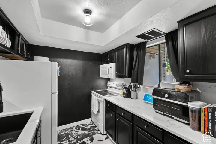 Kitchen featuring dark cabinetry, light countertops, a white refrigerator, a white range, and a ceiling-mounted light fixture