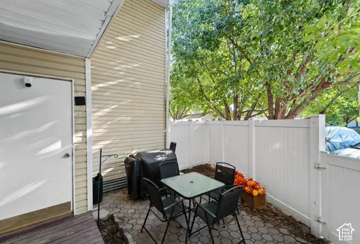 Paved patio area with a privacy fence, wood-finish decking, and light-colored siding