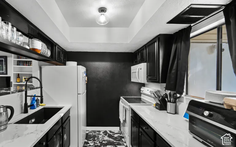 Kitchen featuring black cabinetry, white countertops, a black sink with a matte black pull-down faucet, and white appliances