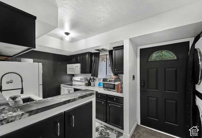 Kitchen with black cabinetry, white appliances, and contrasting countertops