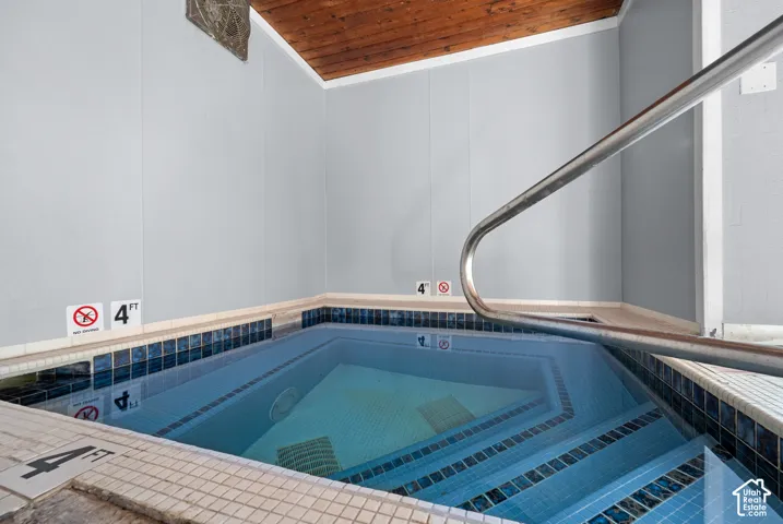 Recessed spa with blue mosaic tile, stainless steel grab rail, and wood-paneled ceiling