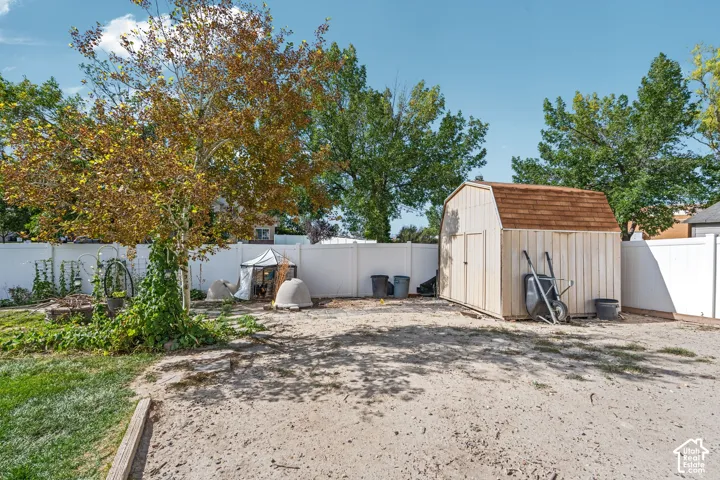Backyard featuring a white vinyl privacy fence, a detached storage shed with a gambrel roof, and mature trees