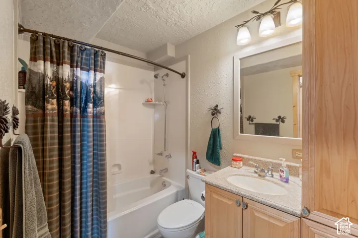 Bathroom featuring a light-wood vanity with speckled stone-composite countertop, integrated oval sink, multi-bulb vanity lighting, and a white acrylic shower-tub surround
