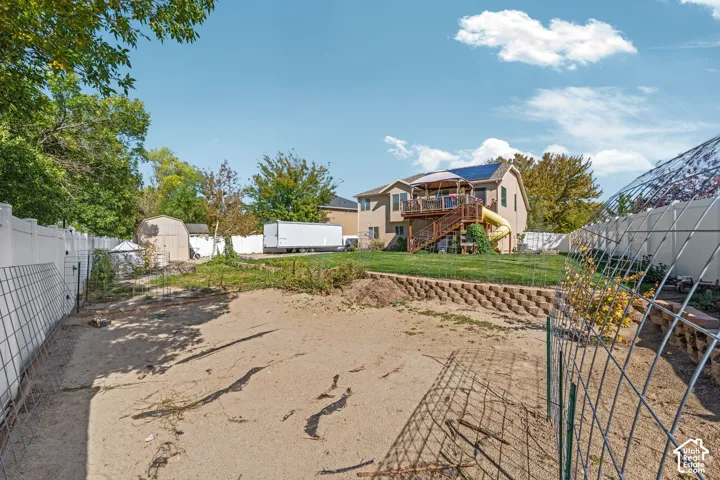 Spacious backyard featuring a multi-level wood deck, solar panels, tiered stone retaining wall, and full-perimeter vinyl fencing