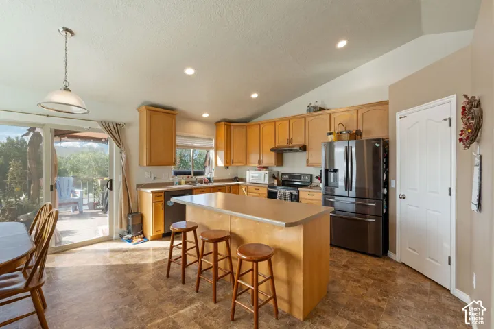 Kitchen featuring light wood cabinetry, central island with an extended countertop, stainless steel refrigerator, recessed lighting, and sliding glass doors