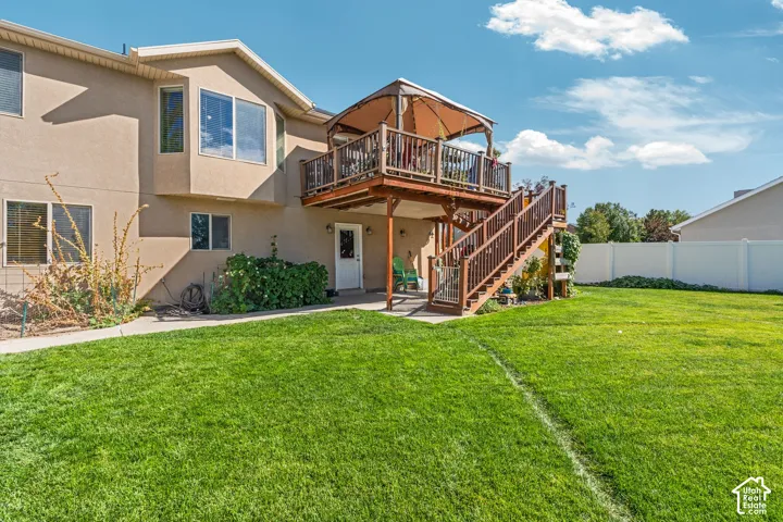 Backyard featuring a raised wood deck with staircase, ground-level concrete patio, and white vinyl privacy fencing