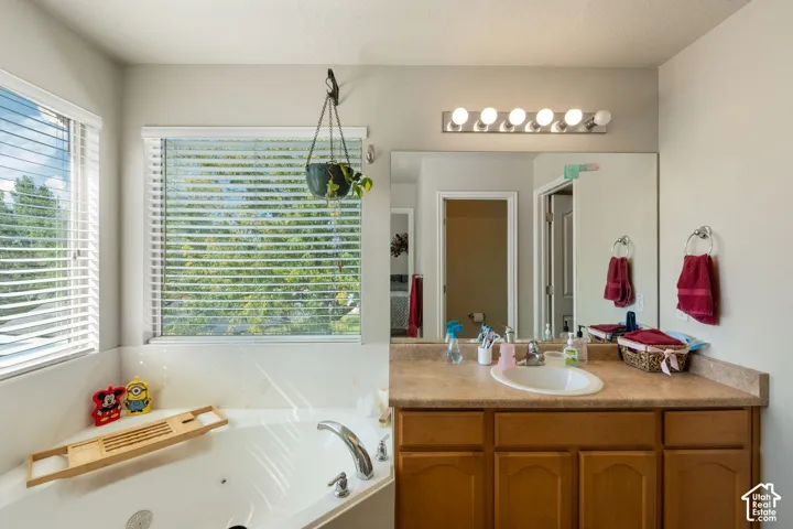 Bathroom featuring a corner jetted soaking tub, wood-finish cabinetry, solid surface countertop with an integrated oval sink, full-width vanity mirror, and five-light wall-mounted fixture