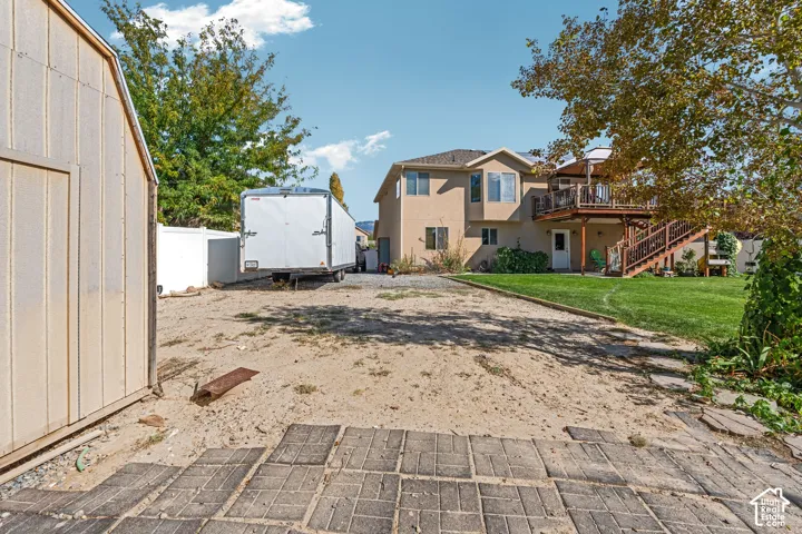 Backyard area featuring a detached storage shed, paver patio, gravel ground cover, manicured lawn, and raised wooden deck with stairs