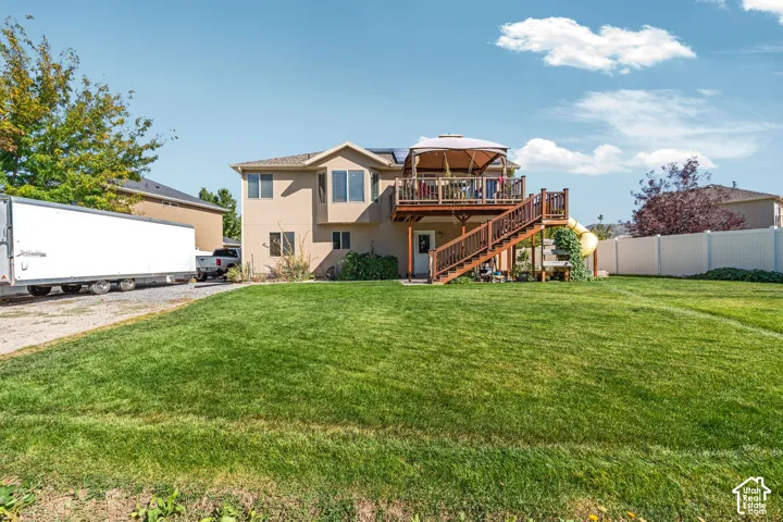 Expansive backyard featuring a manicured lawn, elevated wood deck with stairs, and perimeter vinyl fencing