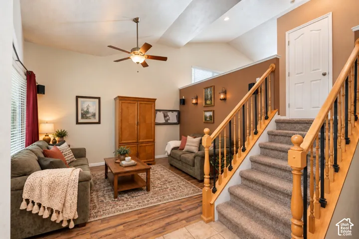 Vaulted ceilings featuring a central paddle ceiling fan, staircase with wood handrails and metal balusters, and wood-finish flooring
