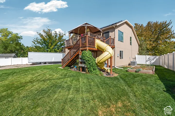 Backyard featuring a raised wood deck with staircase and slide, solar panels, and a perimeter vinyl privacy fence