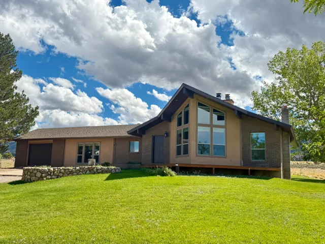 Contemporary exterior featuring a gabled roofline, mixed material facade, expansive windows, a stone-faced retaining wall, and a sloped lawn