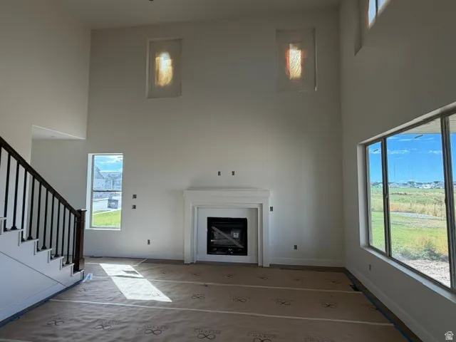 Two-story living area with a fireplace, large windows, and a staircase featuring a dark wood handrail and black balusters