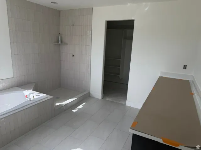 Subway tile shower with integrated shelving, built-in soaking tub, tile flooring, and a countertop vanity space