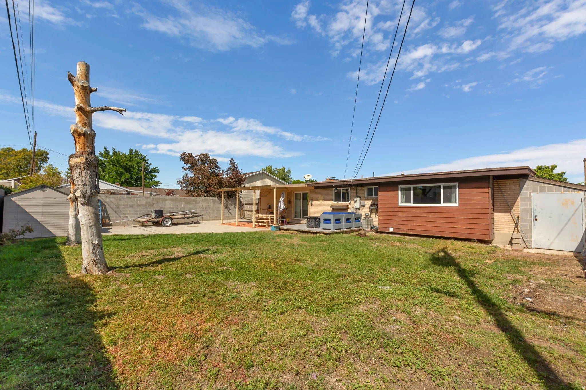 Expansive backyard featuring a concrete patio, a wooden pergola, a storage shed, and a detached garage with a metal door