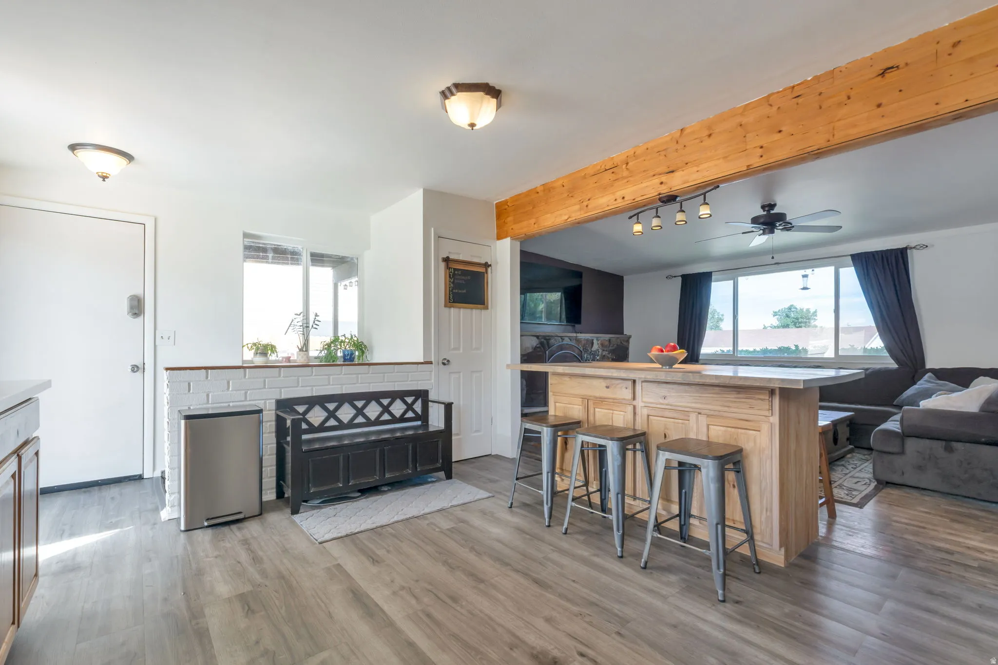 Wood-finish flooring, white brick half-wall, wood beam ceiling, kitchen island with built-in storage, and a ceiling fan