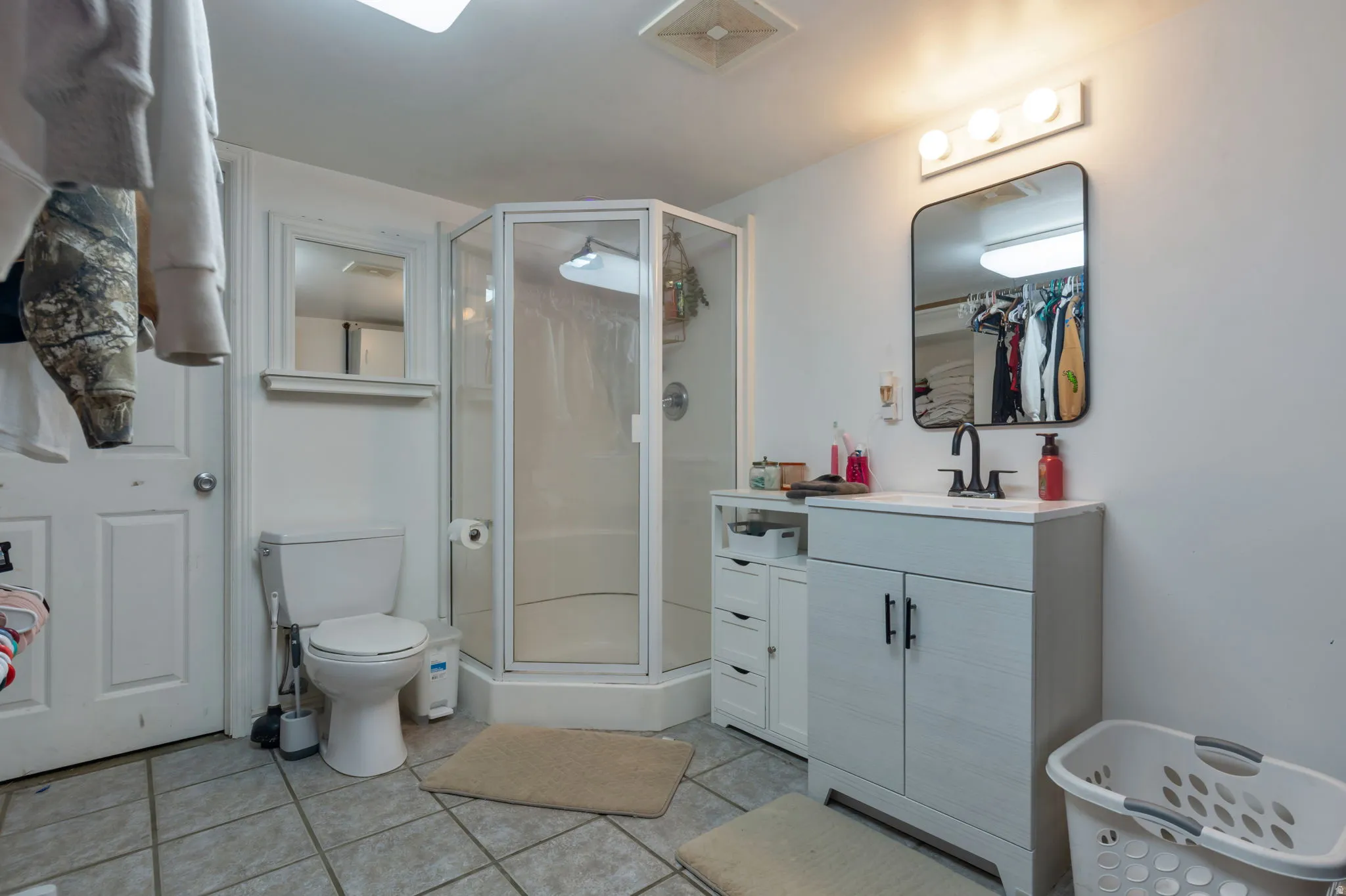 Tiled flooring, corner shower enclosure, single vanity with integrated sink, wall-mounted mirror, and overhead lighting fixture