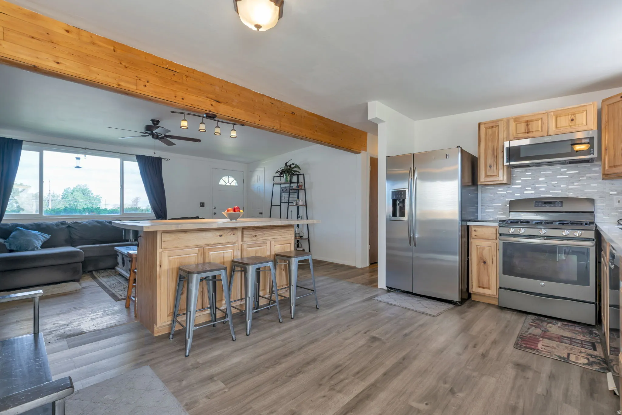 Wood-finish flooring throughout, kitchen island with cabinet storage, stainless steel appliances, light-toned cabinetry, and tile backsplash