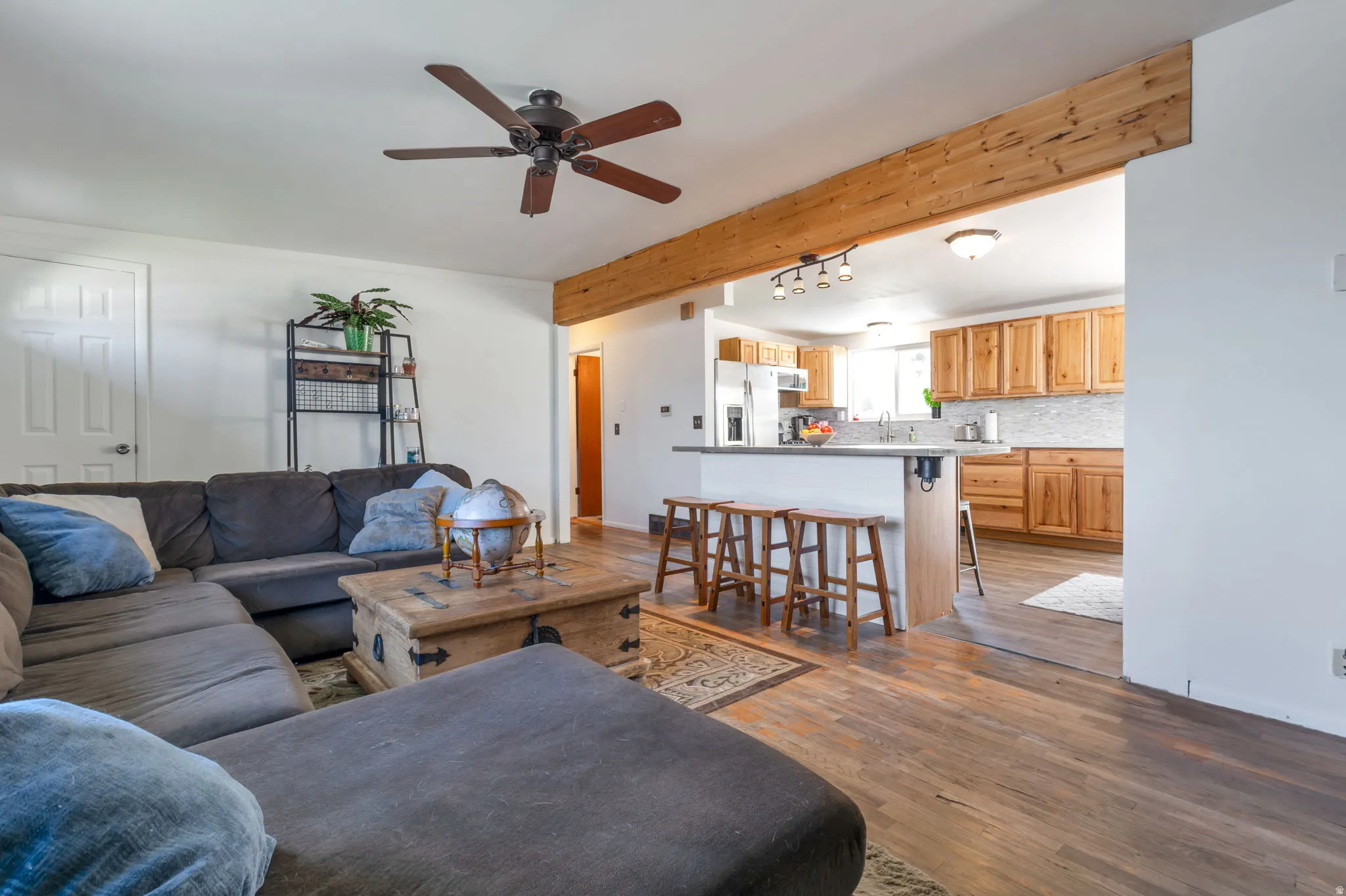 Wood-finish flooring throughout, exposed wood beam, kitchen with wood cabinetry, kitchen island with breakfast bar, and ceiling fan