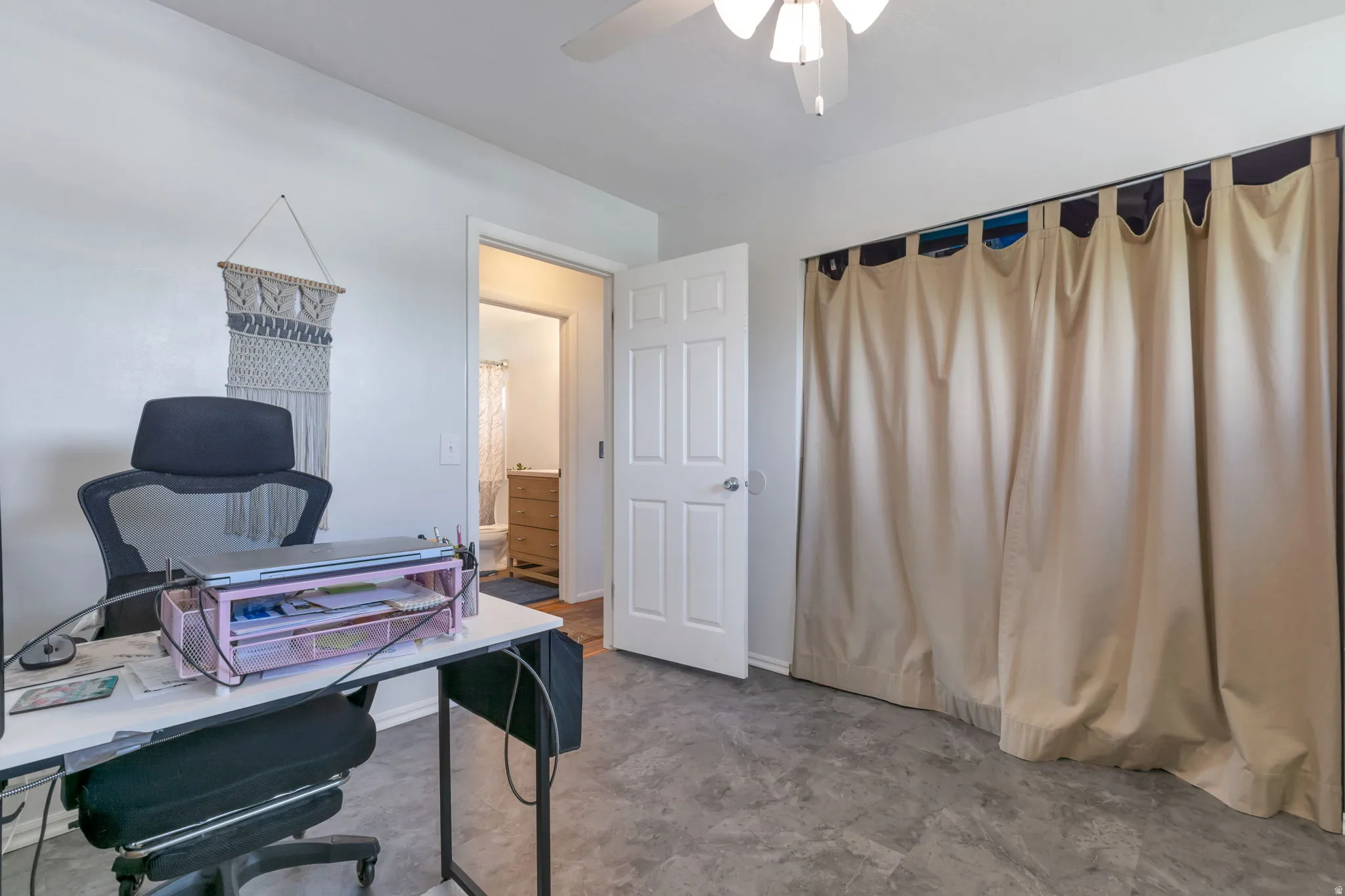 White interior walls, ceiling fan with light fixture, light-toned flooring, white interior door, and a built-in closet with curtain enclosure