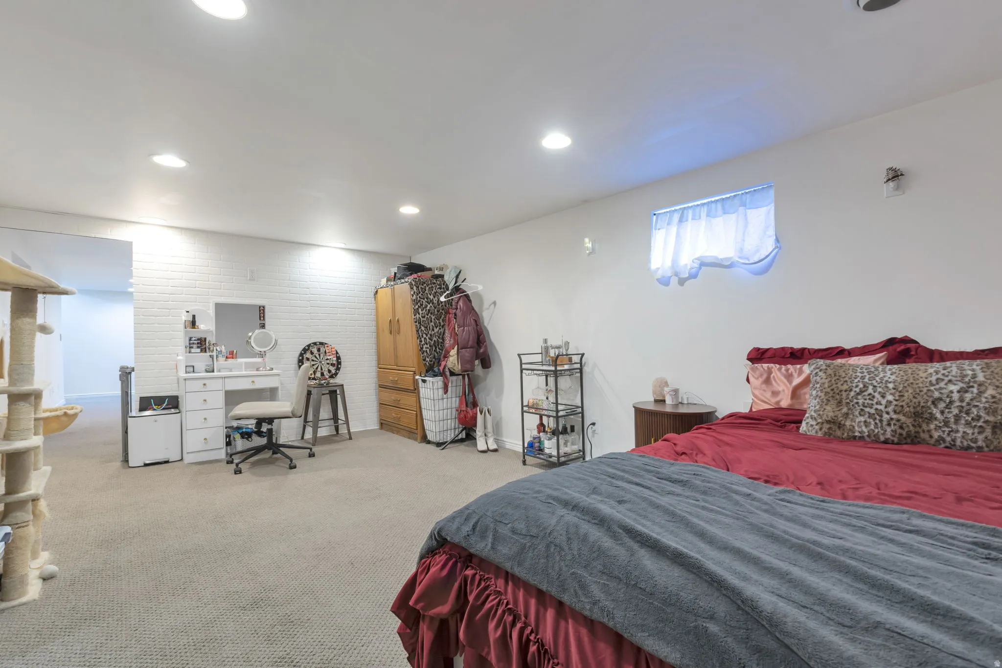Recessed lighting, white painted brick accent wall, carpeted flooring, and a single window