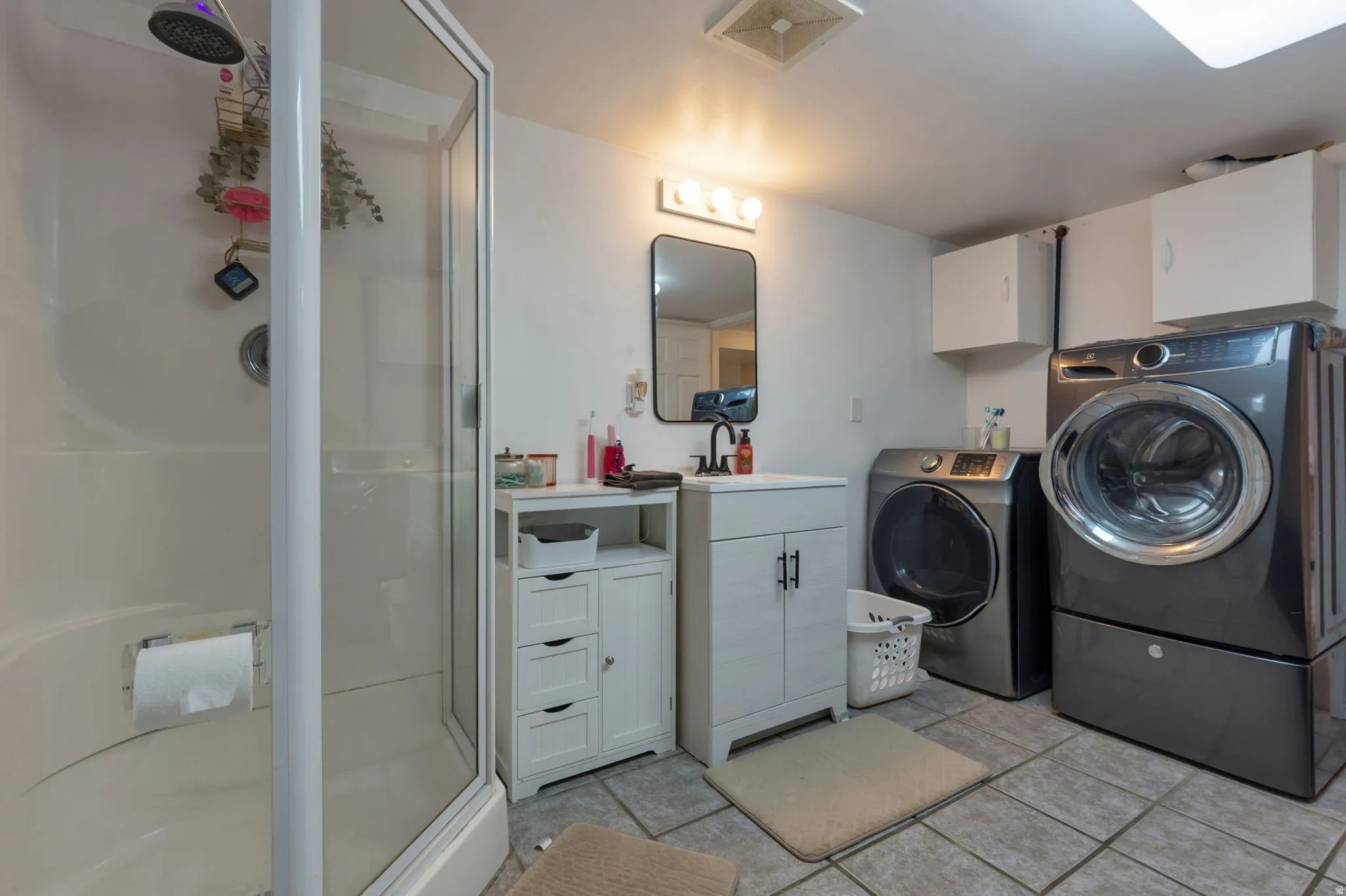 Shower enclosure with clear glass, single vanity with integrated sink, wall-mounted mirror, and tile flooring