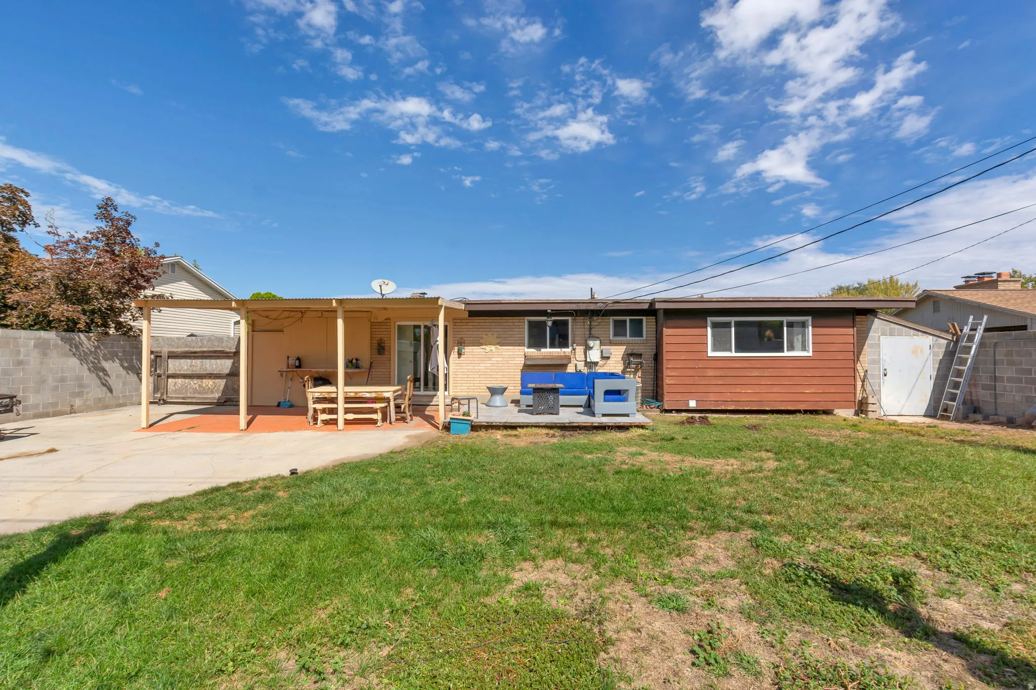 Expansive backyard featuring a covered patio, concrete block fencing, and a separate storage shed with a shingled roof