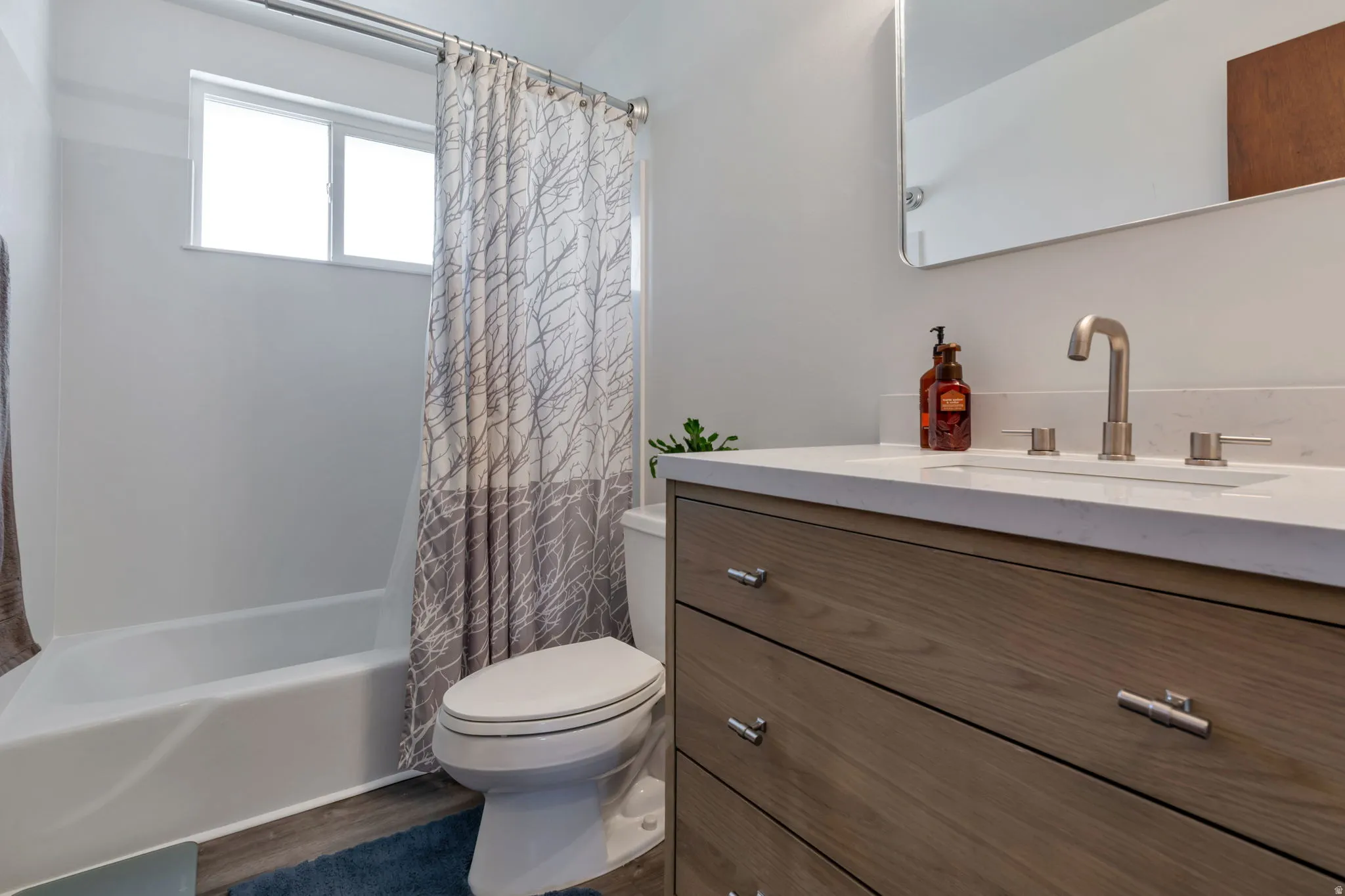 Bathroom featuring a built-in tub, window, wood-finish vanity with drawer storage, integrated sink, and wall-mounted mirror