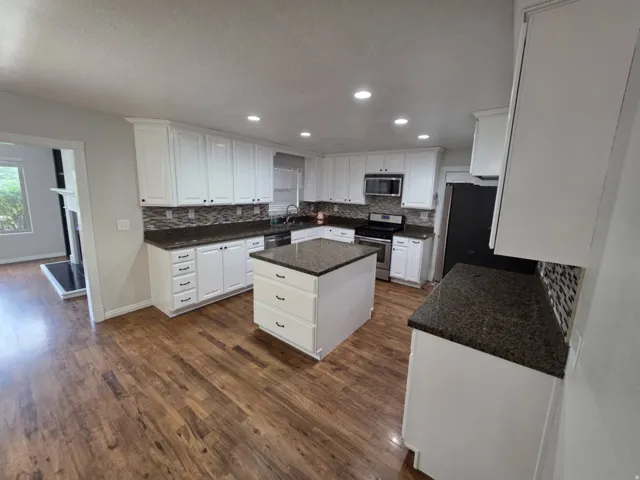 Kitchen featuring a central island, white cabinetry, dark speckled countertops, tile backsplash, and wood-finish flooring