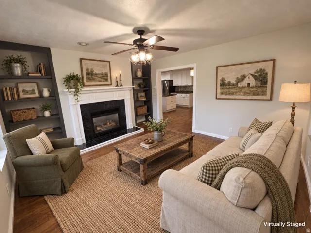 Living area featuring a fireplace with a white mantel and black surround, wood-finish flooring, and a ceiling fan with integrated lighting