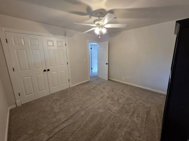 White paneled doors, neutral carpeting, and ceiling fan with lighting