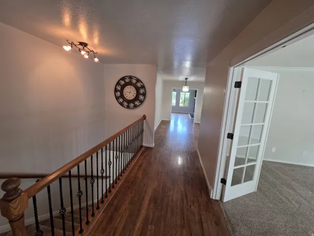 Wood-finish flooring, staircase with wrought iron balusters and wood handrail, track lighting, and French doors