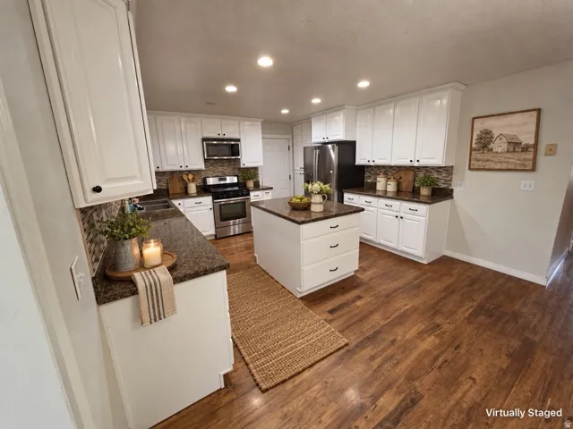 Kitchen featuring wood-finish flooring, white cabinetry, a central island, dark countertops, and stainless steel appliances