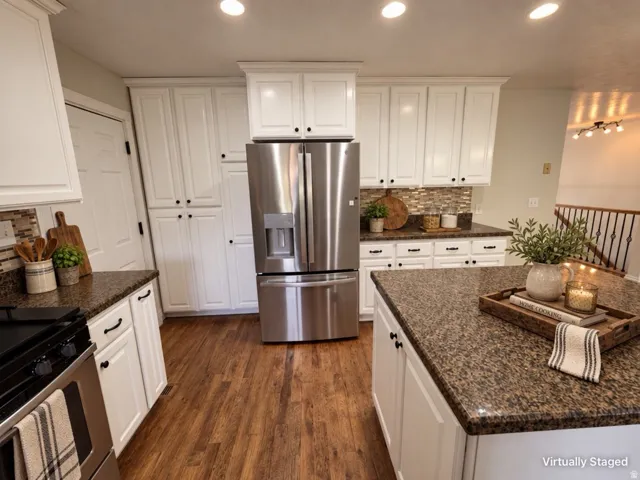 White cabinetry, stainless steel appliances, wood-finish flooring, mosaic tile backsplash, and dark speckled countertops