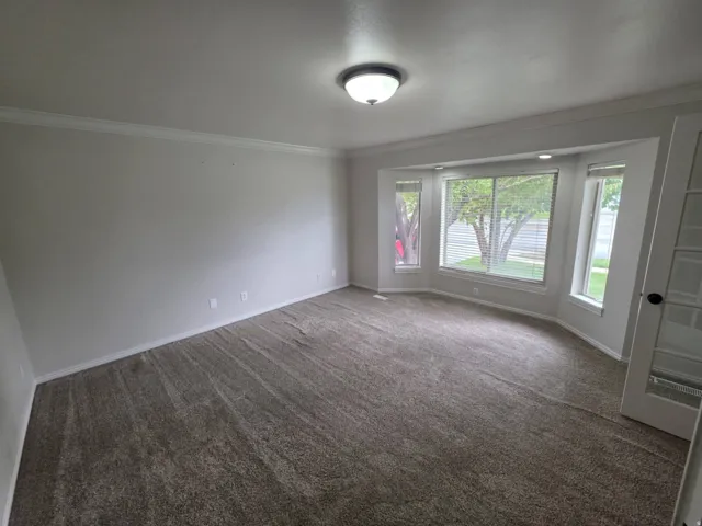 Recessed lighting, crown molding, bay window, light neutral wall paint, and gray textured carpeting