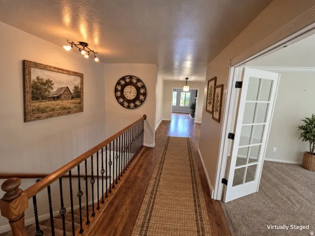 Wood-finish flooring with a textured runner, white paneled French doors, and an ornate wrought iron and wood banister