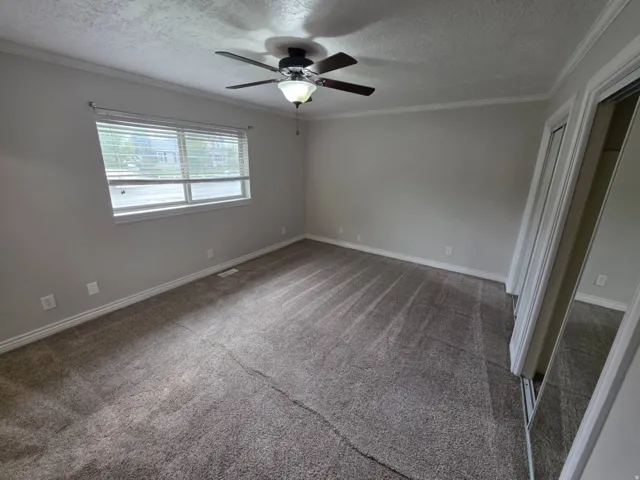 Neutral-toned carpet flooring, a ceiling fan with integrated lighting, and crown molding detail
