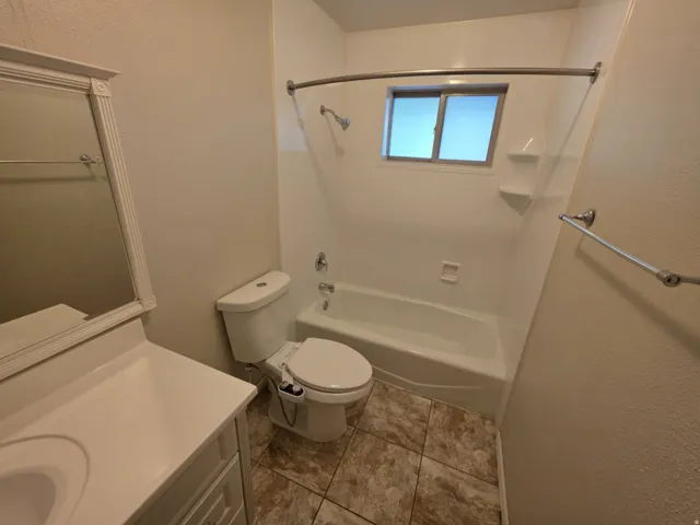 White vanity with an integrated sink, framed mirror, tiled flooring, and a bathtub with a shower