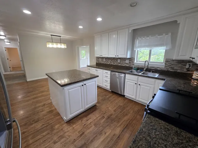 Kitchen featuring white cabinetry, dark speckled countertops, a tile backsplash, wood-finish flooring, and a central island