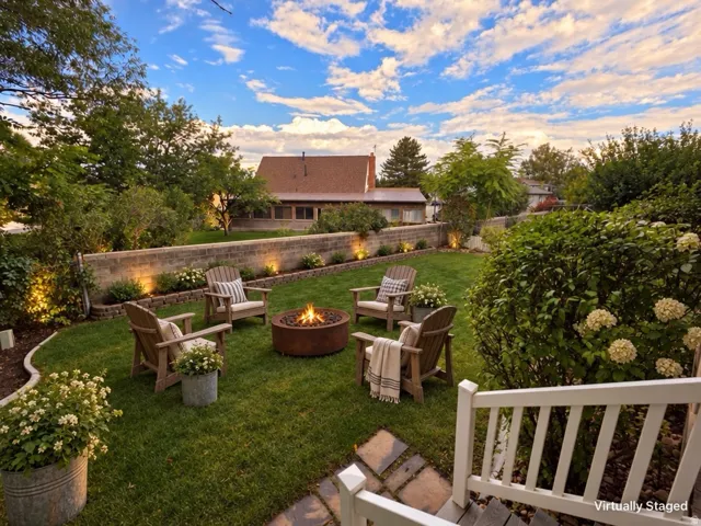 Landscaped backyard featuring a stone retaining wall with integrated lighting, a manicured lawn, and a built-in fire pit