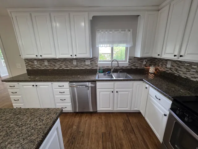 White cabinetry with dark hardware, stone-finish countertops, stainless steel appliances, mosaic tile backsplash, and wood-finish flooring